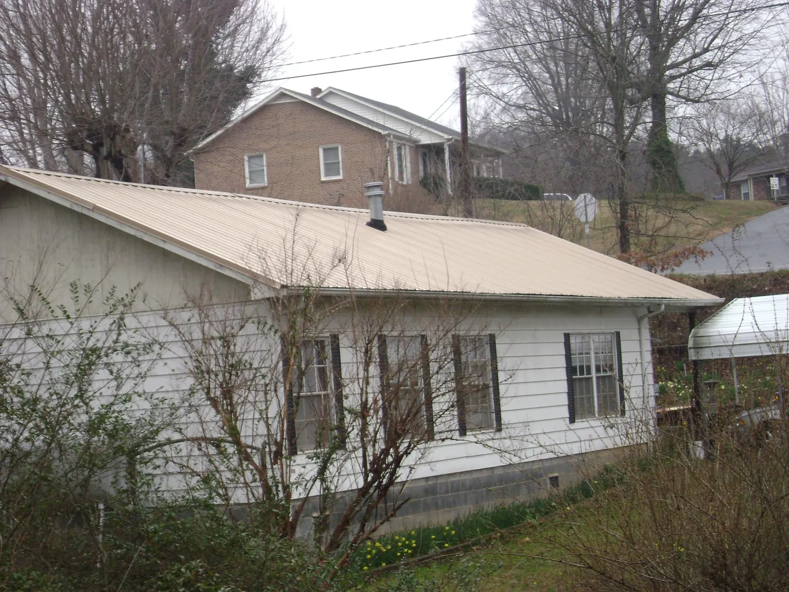Tan metal roof on a white sided house set into a hillside — Commercial Roofing by Roofing Brothers in Fremont